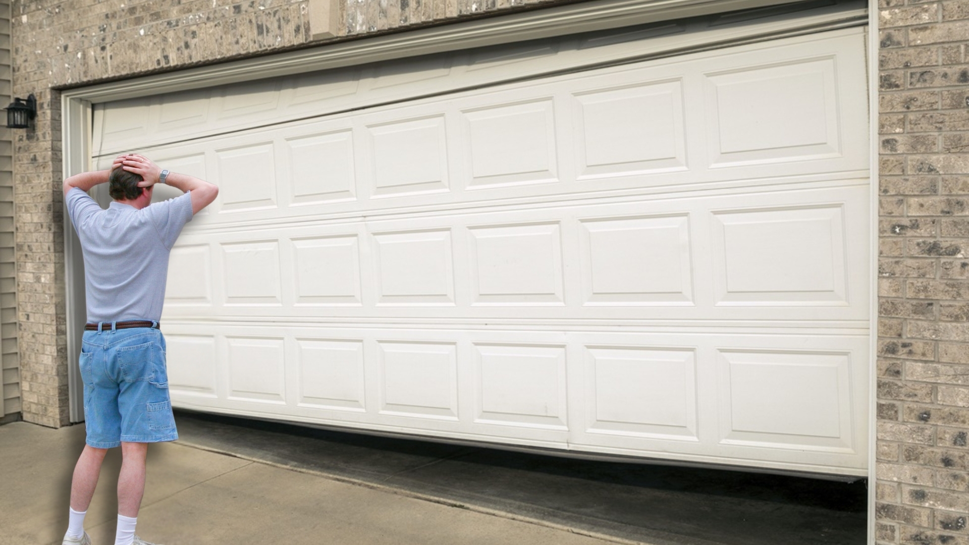 A homeowner looking at a crooked garage door stuck in place.